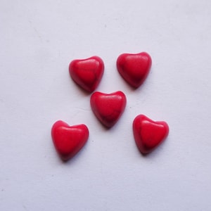 May include: Five red heart-shaped beads with a slightly textured surface. The beads are arranged on a white background. These heart-shaped beads are suitable for jewelry making and crafting projects.