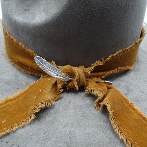 May include: A gray felt hat with a brown velvet ribbon tied around the crown. A silver feather pin is attached to the ribbon.