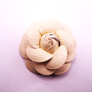 May include: A cream-colored leather flower brooch with a textured surface.