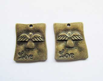 May include: Two bronze-colored rectangular pendants with an angel design and the word "Love" embossed on each. The pendants have a hole at the top for stringing. The angel has outstretched wings.