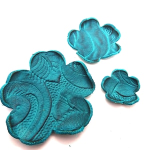 May include: Three teal blue leather flower shapes with a textured design.
