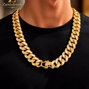 Puede incluir: Un collar de cadena gruesa en tono dorado con eslabones entrelazados que presentan un patrón texturizado de corte de diamante en la superficie. El collar incluye un mecanismo de cierre rectangular seguro. El logo ZarishaJewels es visible arriba.