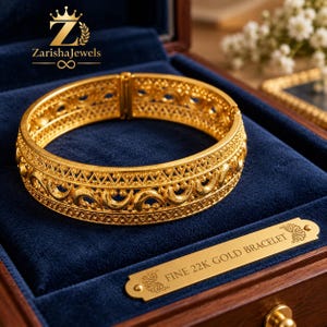 Puede incluir: Una pulsera de oro de 22 quilates con un intrincado patrón de filigrana que presenta formas de media luna repetitivas y bordes texturizados. La pulsera se exhibe en una caja forrada de terciopelo azul con una placa dorada FINE 22K GOLD BRACELET.