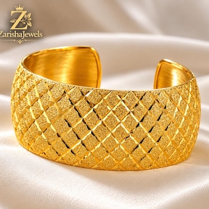 Puede incluir: Un brazalete ancho de oro con una superficie texturizada de patrón de diamantes en el exterior. El interior del brazalete es liso y pulido. El logotipo de ZarishaJewels es visible en la esquina superior izquierda de la imagen.