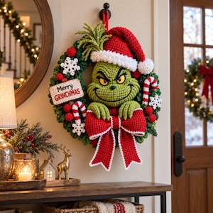 Peut inclure: Une couronne en crochet représentant un personnage vert avec un bonnet de Père Noël rouge, un grand nœud rouge, des sucres d'orge et des flocons blancs. Une pancarte rectangulaire affiche le texte Merry GRINCHMAS en rouge et noir.