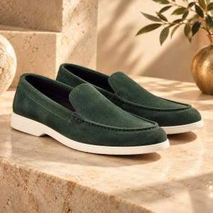 May include: A pair of dark green suede loafers featuring a moccasin-style stitched toe seam and a solid white rubber sole. The shoes have a low-cut silhouette with a smooth, matte finish on the upper material and a clean, minimalist design.