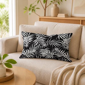 May include: A rectangular throw pillow featuring a high-contrast black background with a repeating white palm leaf pattern. The leaves have a distressed, textured appearance, creating a bold graphic design across the entire surface of the pillow.