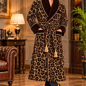 Pode incluir: Um roupão de pelúcia até o joelho com estampa de leopardo marrom e preto, gola xale acolchoada marrom escura, punhos combinando e dois bolsos frontais. O roupão inclui um cinto com borlas douradas e o texto ROVIQUEAPPAREL.