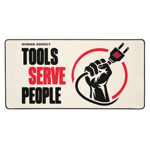 May include: A rectangular desk mat with a cream background and black border. The text reads HUMAN AGENCY TOOLS SERVE PEOPLE in black and red. A graphic of a black fist holding a black electrical plug is centred within a red circular line.