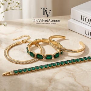 Puede incluir: Un conjunto de tres pulseras doradas con piedras rectangulares de color verde esmeralda y cristales pavé transparentes. Incluye una pulsera de cadena flexible con piedras verdes, un brazalete rígido con piedras verdes y un brazalete pavé fino.