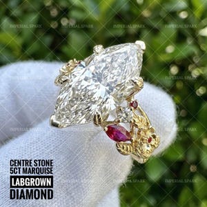 May include: A gold ring featuring a large 5ct marquise-cut lab-grown diamond centre stone. The band is decorated with gold leaves, small round diamonds, and marquise-cut red rubies. Text on the image reads: CENTRE STONE 5CT MARQUISE LABGROWN DIAMOND.