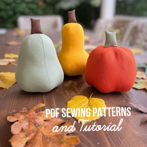 Pode incluir: Três abóboras de tecido nas cores verde sálvia, amarelo brilhante e laranja, cada uma com um caule castanho ou cinzento. As abóboras são arredondadas e segmentadas. O texto PDF SEWING PATTERNS and Tutorial está sobreposto em letras brancas.