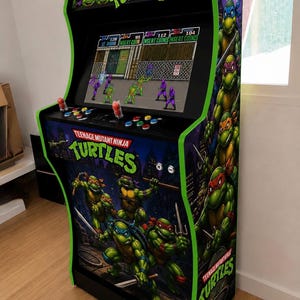 Puede incluir: Una máquina recreativa de Teenage Mutant Ninja Turtles con una pantalla que muestra el juego, un panel de control con joysticks y botones de colores, y paneles laterales decorados con gráficos. El mueble tiene un marco negro con bordes verdes.