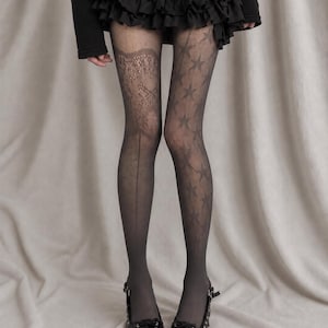 May include: Black patterned tights featuring a sheer star design on one leg and a floral lace-like panel on the other, paired with a black ruffled mini skirt and black pointed-toe lace-up shoes with a buckle strap detail.