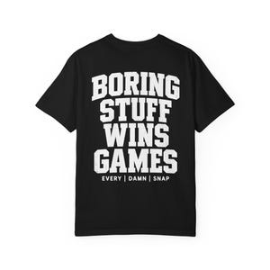 May include: A black short-sleeve t-shirt featuring white distressed-style block lettering on the back that reads BORING STUFF WINS GAMES followed by the text EVERY | DAMN | SNAP in a smaller, clean sans-serif font centered below the main phrase.