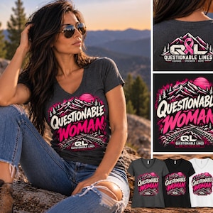 May include: A charcoal grey V-neck t-shirt featuring a graphic print of mountains, a pink sun, and the text "QUESTIONABLE WOMAN" in white and pink lettering, with "QL QUESTIONABLE LINES" printed below the design in a smaller font.