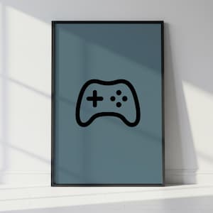May include: A framed poster featuring a black outline of a video game controller on a teal background. The controller design includes a cross-shaped directional pad and several buttons. The frame is black, and the poster is leaning against a white wall.