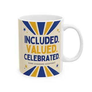 May include: A white ceramic mug featuring a graphic design with blue and yellow sunburst rays. The text reads INCLUDED. VALUED. CELEBRATED. DOWN SYNDROME ACCEPTANCE in blue and yellow lettering, accented by small blue and yellow star icons.