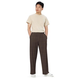 Puede incluir: Una camiseta beige de manga corta y cuello redondo combinada con pantalones de color marrón oscuro con un sutil patrón de cuadrícula en marrón más oscuro. Los pantalones tienen un corte recto y relajado con cintura elástica, junto a sandalias blancas.