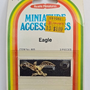 May include: Vintage package of miniature eagle accessories. The package features a rainbow-colored arch design and the words "MINIATURE ACCESSORIES" and "Eagle". Two gold-colored eagle miniatures are visible.