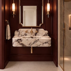 Puede incluir: Un lavabo de pared con una encimera de mármol blanco con vetas de color púrpura oscuro, complementado con un grifo y manijas doradas. Sobre el lavabo hay un espejo con marco dorado flanqueado por dos lámparas de pared cilíndricas verticales.
