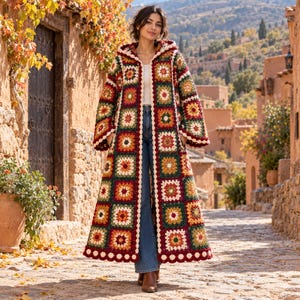 Pode incluir: Um cardigã longo de crochê com capuz, apresentando um patchwork de quadrados de vovó multicoloridos em tons de vermelho profundo, verde floresta, amarelo mostarda e creme. A peça tem mangas compridas, frente aberta e borda festonada.