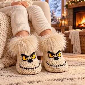 Puede incluir: Un par de pantuflas de ganchillo color crema con un rostro de personaje que tiene ojos amarillos, pupilas negras y una boca negra cosida. Las pantuflas están rematadas con un borde grueso y esponjoso de piel sintética color crema.