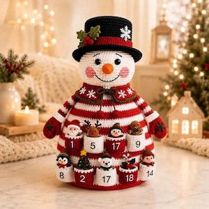 May include: A crocheted snowman advent calendar featuring a black top hat with holly and a snowflake, a white body with red and white horizontal stripes, and eight small pockets labeled with numbers 1, 2, 5, 8, 9, 14, 17, and 18.