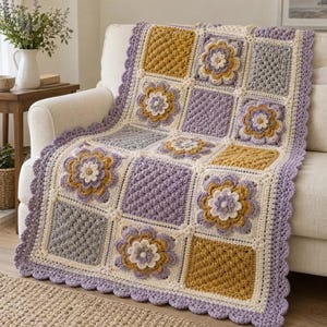May include: A handmade crochet blanket featuring a square-patterned design with alternating blocks of mustard yellow, lavender, and light gray yarn. The blanket includes raised floral motifs and a scalloped lavender border edge.