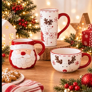 May include: Three ceramic mugs featuring holiday designs. One mug is shaped like a smiling Santa Claus with a red hat. A tall white mug features a reindeer and red snowflakes. A wide white mug displays a reindeer face with brown antlers.