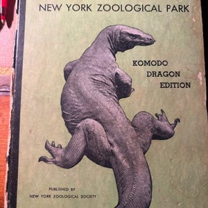 May include: A vintage guidebook titled Official Guide New York Zoological Park Komodo Dragon Edition. The light green cover features a large black illustration of a Komodo dragon, with text indicating it was published by the New York Zoological Society.