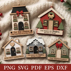 Peut inclure: Cinq décorations de Noël en bois en forme de maison avec des attaches en ficelle. Les modèles incluent une maison au toit noir avec 2026, une maison rouge avec une couronne, une maison blanche avec un cœur, une grise avec un flocon et une verte.