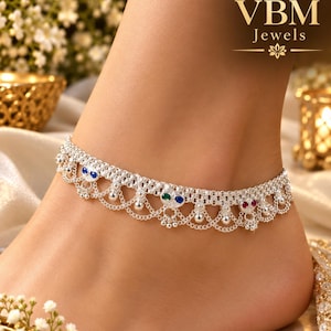 May include: A silver anklet featuring a delicate chain design with small dangling beads and embedded blue, green, and red stones. The jewelry piece is displayed with the VBM Jewels logo visible in the upper right corner of the frame.