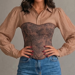 May include: A beige long-sleeved button-down shirt with a textured fabric, worn under a dark brown corset featuring a black floral pattern. The outfit is paired with a blue denim mini skirt, creating a layered look with contrasting textures and colors.