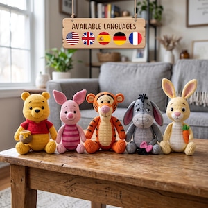 May include: Five crocheted stuffed animals arranged in a row on a wooden table. The characters include a yellow bear in a red shirt with a honey pot, a pink piglet, an orange and black striped tiger, a grey donkey, and a yellow rabbit holding a carrot.