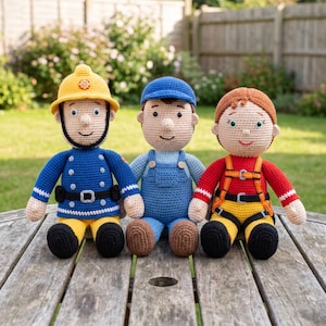 Puede incluir: Tres muñecos tejidos a mano en crochet que representan a un bombero con casco amarillo y uniforme azul, un personaje con peto azul y gorra, y un personaje con camisa roja de manga larga, pantalones amarillos y un arnés de seguridad negro y naranja.