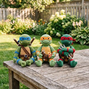 May include: Three crocheted turtle dolls with green skin and tan shells. The left doll wears a blue mask and carries two katanas. The center doll wears an orange mask and holds a slice of pizza. The right doll wears a red mask and holds two sai.
