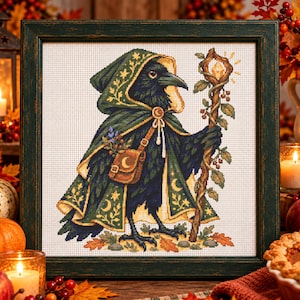 May include: A framed cross-stitch embroidery featuring a black crow wearing a dark green hooded cloak with gold celestial patterns, carrying a brown leather satchel and holding a wooden staff topped with a glowing amber crystal.