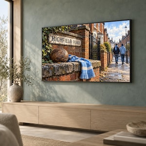 May include: A television screen displaying a scene of a vintage brown leather football and a blue and white striped scarf resting on a brick wall with a sign reading HIGHFIELD ROAD, with a street view of two people walking in the background.