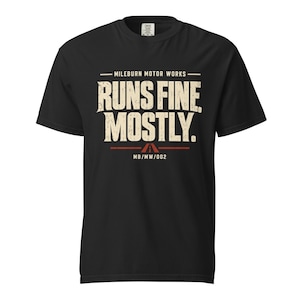 Puede incluir: Una camiseta negra de manga corta con el texto "MILEBURN MOTOR WORKS" sobre las palabras "RUNS FINE. MOSTLY." en una fuente crema desgastada. Debajo del texto hay una línea horizontal roja con un icono de carretera y el código "MB/MW/002".