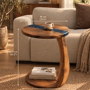 May include: A round wooden side table with a blue resin inlay, featuring a curved support base and a lower shelf holding two books. The table measures 39 cm in diameter, 56.5 cm in height, and 53 cm at the base width.