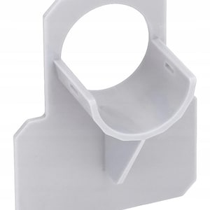 Puede incluir: Un soporte de montaje de plástico gris claro que presenta una base rectangular plana con una abertura circular integrada y un soporte de cuna semicircular que sobresale. El componente tiene un acabado liso y una estructura rígida.