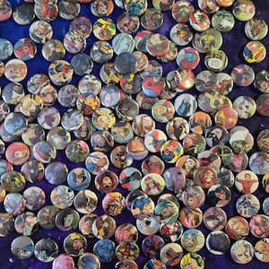 May include: A large collection of circular pin-back buttons featuring various colorful comic book character illustrations, including superheroes and villains, scattered across a dark blue surface with a visible texture.