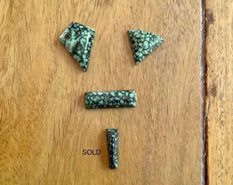 Puede incluir: Cuatro cabujones de turquesa pulidos con un patrón de matriz oscuro. El conjunto incluye una pieza en forma de cometa, una pieza triangular, una pieza rectangular y una pequeña pieza cónica con la palabra SOLD impresa al lado.
