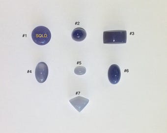 Puede incluir: Siete piedras preciosas moradas sueltas dispuestas en una cuadrícula, numeradas del #1 al #7. El artículo #1 es un cabujón redondo con el texto SOLD. Los artículos #2, #4, #5 y #6 son cabujones ovalados. El #3 es rectangular y el #7 es triangular.