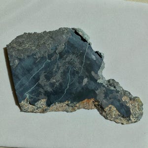 May include: A dark gray rock with a rough, irregular shape. The rock has a metallic sheen and is covered in small, white crystals.