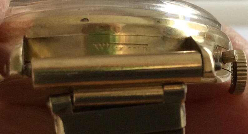 May include: A gold-toned wristwatch with a black leather band. The watch face is not visible in the image. The watch has the word "Waltham" engraved on the side.