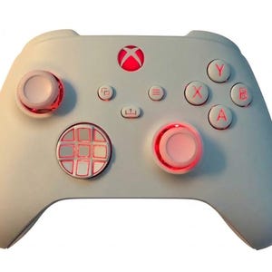 May include: A white wireless video game controller featuring a central Xbox logo button, two analog sticks, a directional pad, and action buttons labeled A, B, X, and Y. The controller includes red LED backlighting around the sticks and buttons.