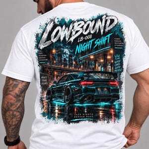 May include: A white t-shirt featuring a large back graphic of a dark sports car parked at a gas station at night. The design includes the text "LOWBOUND", "NIGHT SHIFT", "LB-008", "FUEL PASSION DRIVES FREEDOM", "SAME ROADS DIFFERENT STORIES", "NIGHTS CREATE LEGENDS", and "LATE NIGHTS BETTER DAYS".