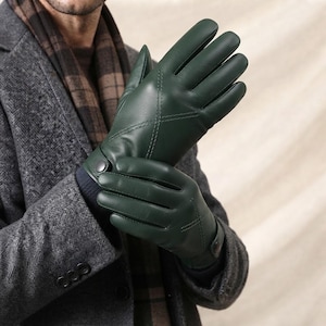 May include: A pair of dark green leather gloves featuring decorative stitching on the back of the hand and a small snap button closure at the wrist. The gloves have a smooth finish and are worn over a dark blue ribbed cuff, visible at the wrist.